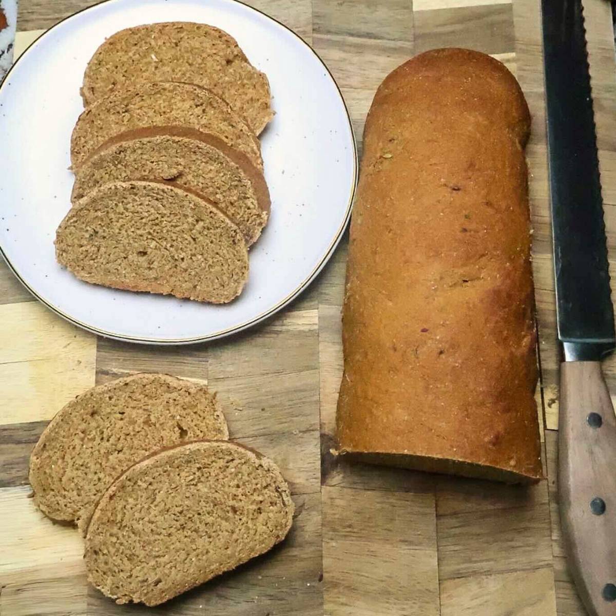 A white plate of sliced bread next to the partially sliced loaf on a wood board with knife.