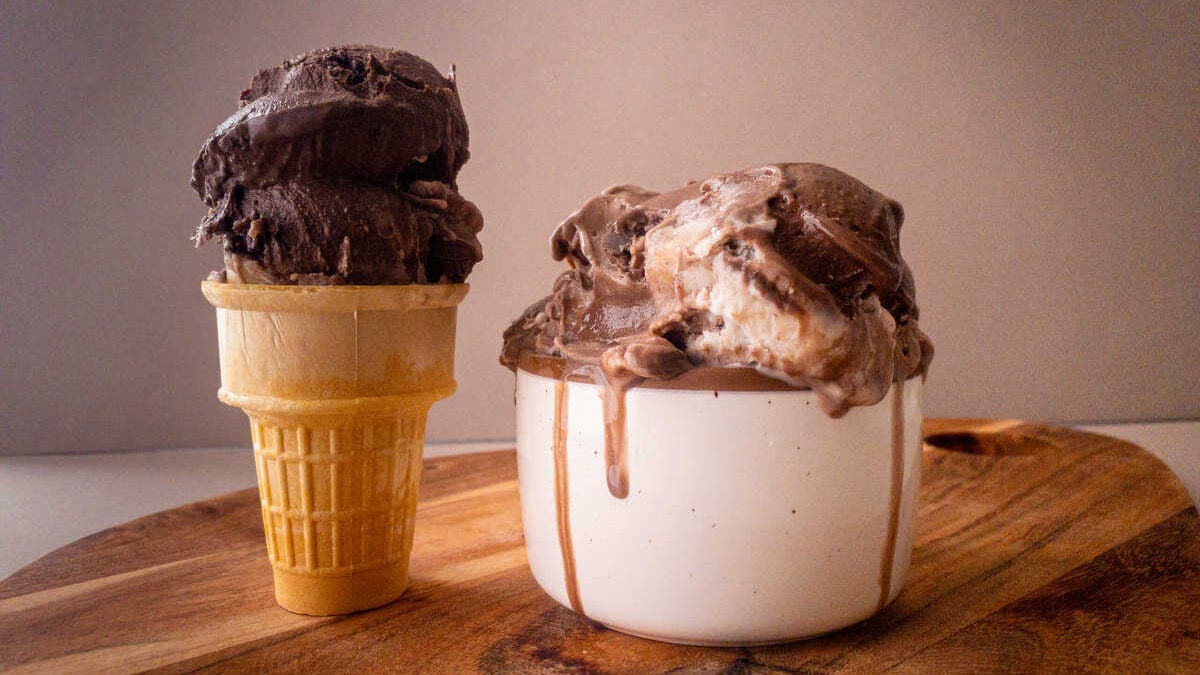 A cone and a dish of the chocolate-coconut swirl ice cream on a wooden board.