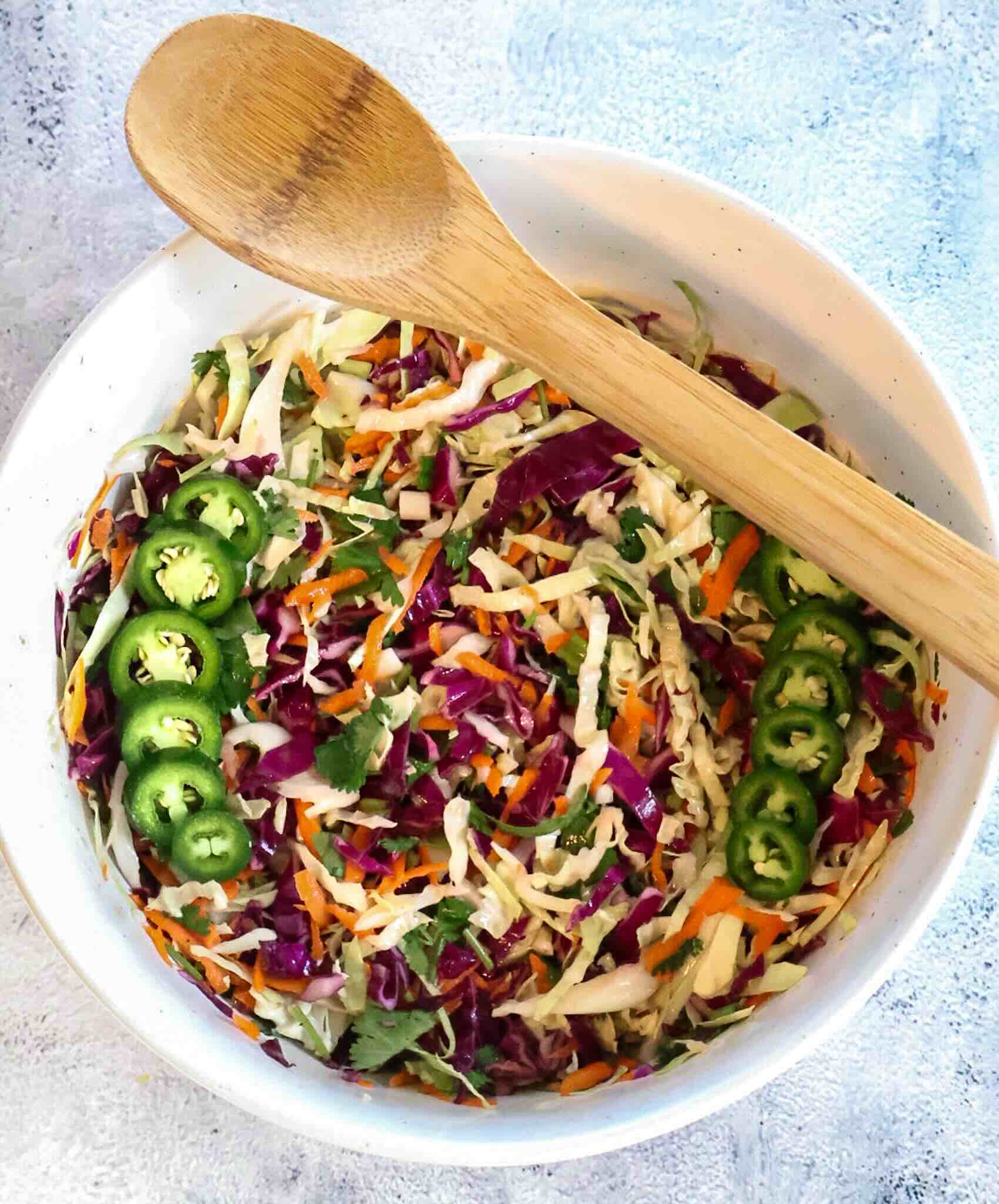 Large bowl of cilantro jalapeño coleslaw with wooden spoon on gray background.