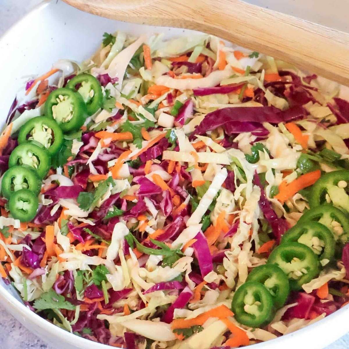 A white bowl with cilantro lime coleslaw and a wooden spoon resting on the edge.
