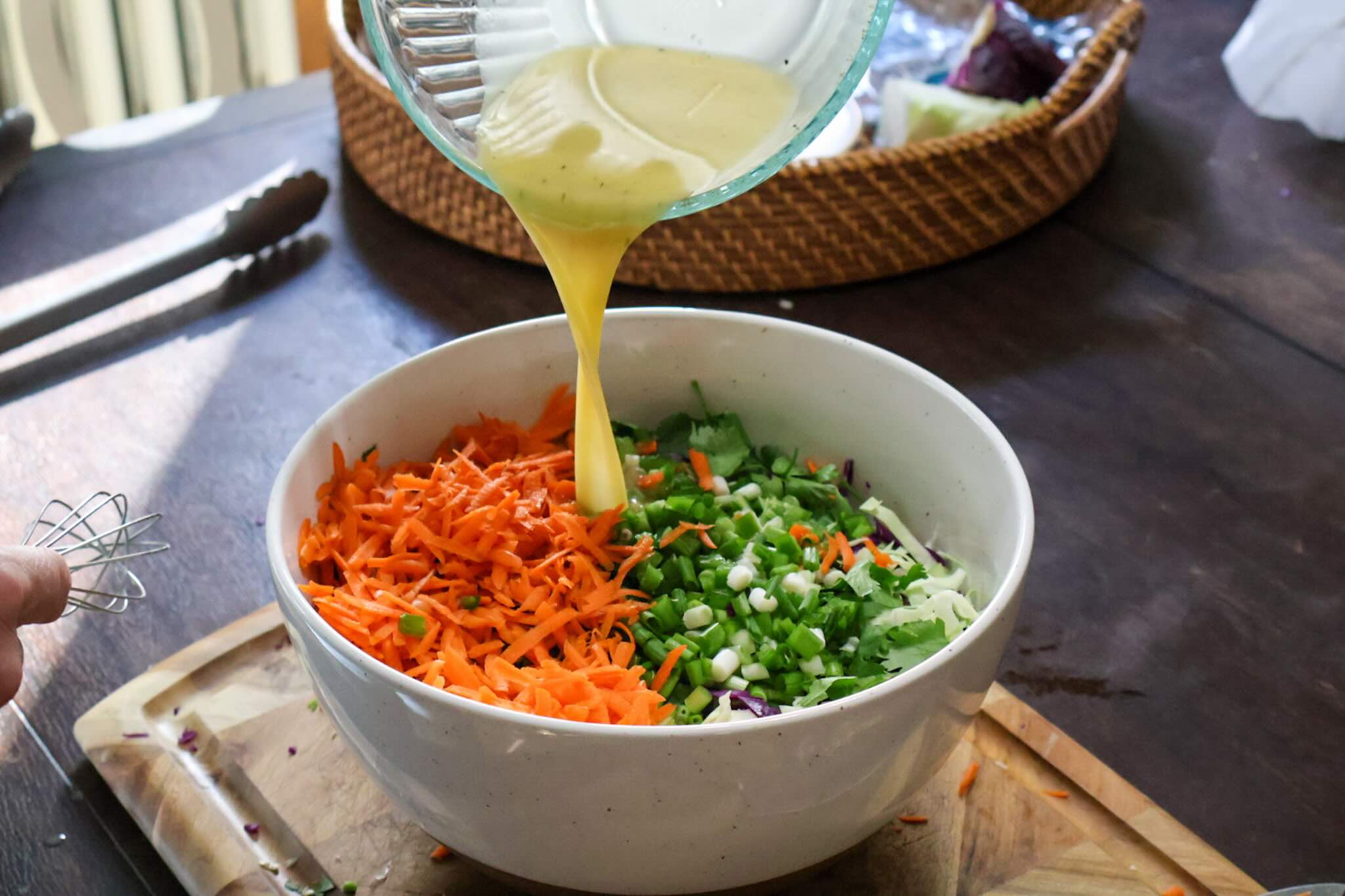Pouring vinaigrette over the coleslaw in a large white bowl.
