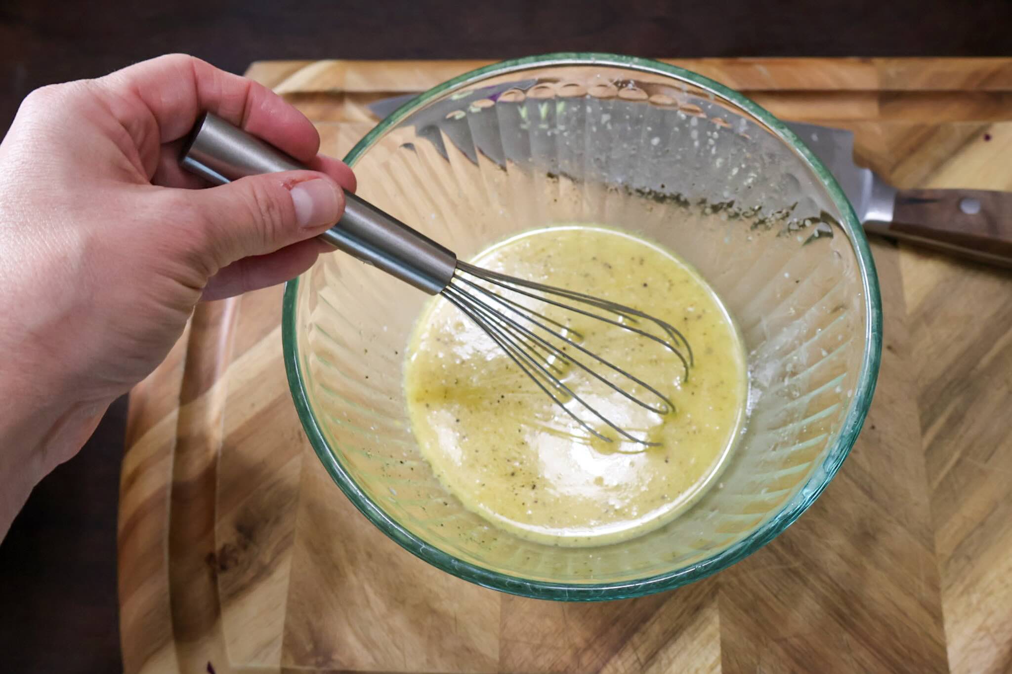 Whisking the vinaigrette in a glass bowl on a wooden cutting board.