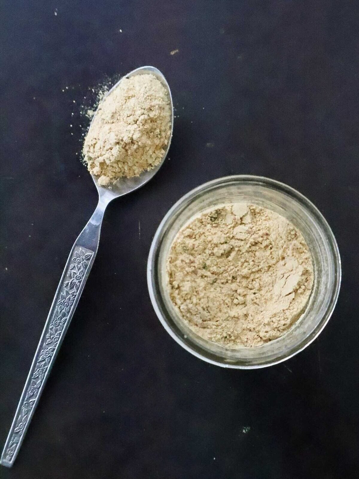 A jar of seasoning with a spoonful of seasoning on black background.